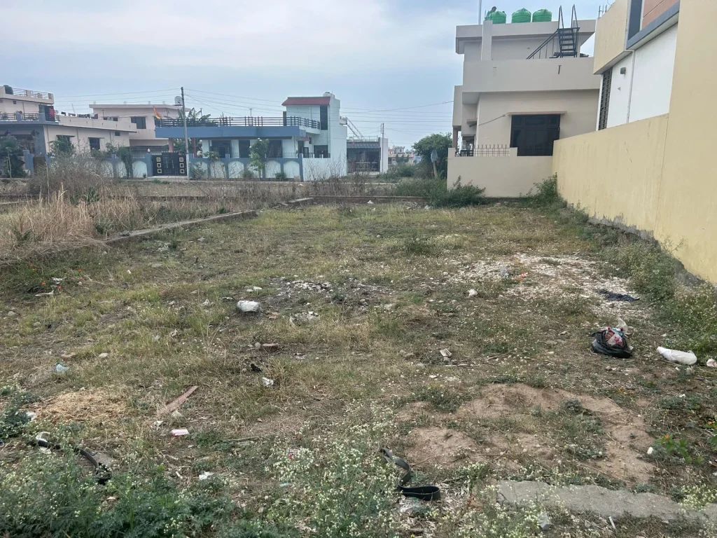 Open empty plot of land with a green metal fencing frame and distant trees in Haldwani by RRB Properties & Construction
